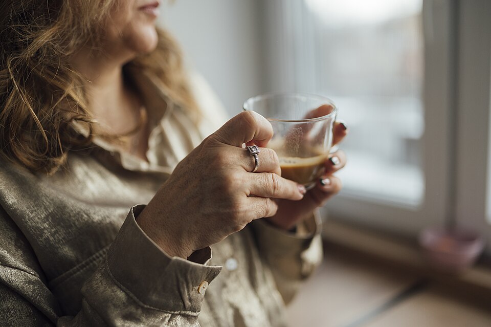 窓辺でコーヒーのグラスを持つ手